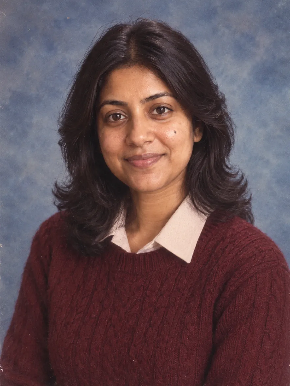 An adult woman in a burgundy sweater against a blue-gray yearbook backdrop